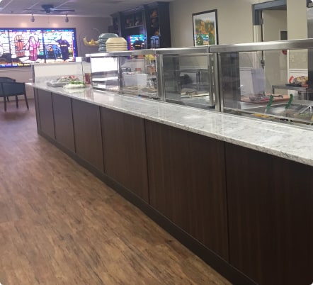 Empty cafeteria serving counter with stained glass background.