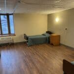 Empty dormitory room with single bed and wooden furniture.