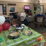 Senior living room with residents watching TV, festive decor.