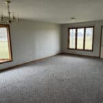 Empty room with large windows and carpet flooring.