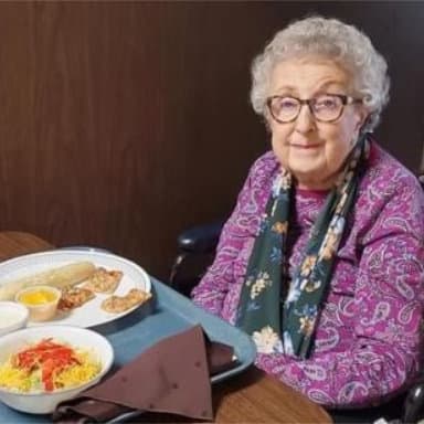 Elderly woman smiling with meal at a table