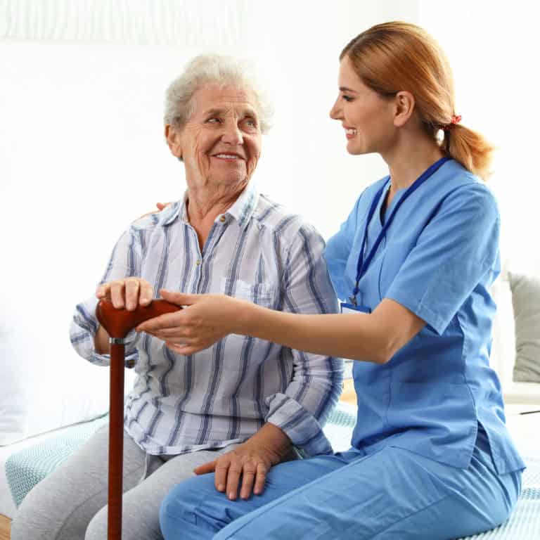 Elderly woman with caregiver smiling, holding walking cane.