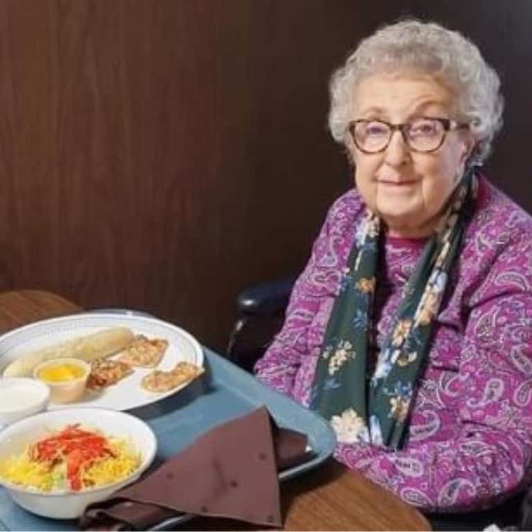 Elderly woman dining, smiling with meal on table