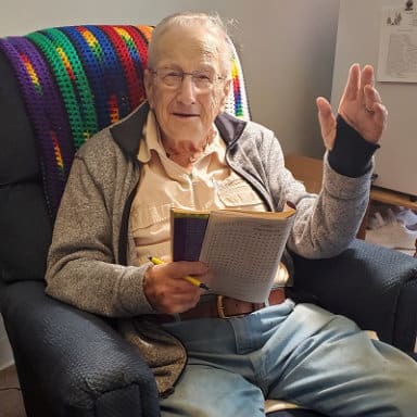 Elderly man waving while reading in a chair.