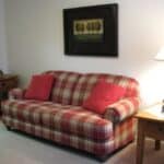 Plaid sofa in living room with framed art and lamp.